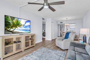 Ein Wohnzimmer mit Fernseher, Holzschrank, grauem Sofa und Deckenventilator.