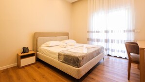 A bedroom with a bed, bedside table, chair, and a window with curtains. - Toro Double Room With City View (Durrës)