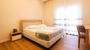 A hotel room with a bed, a desk, a chair, a bedside table, and a telephone. - Toro Double Room With City View (Durrës)