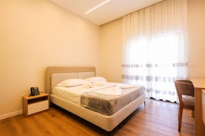 A hotel room with a bed, a desk, a chair, a bedside table, and a telephone. - Toro Double Room With City View (Durrës)
