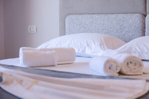 Ein ordentlich bezogenes Bett mit weißen Leinen und aufgerollten Handtüchern.