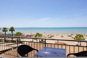 A beach view from a balcony with chairs and a table, palm trees, and umbrellas on the sand. - Toro Family Room With Sea View (Durrës)