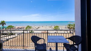 Een balkon met twee stoelen en een tafel met uitzicht op een strand met parasols en mensen.