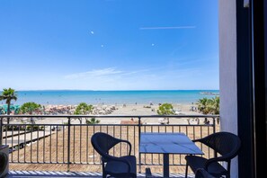 A balcony with two chairs and a table overlooking a beach with umbrellas and people. - Toro Family Room With Sea View (Durrës)