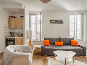 Ein zeitgemäßer Wohnbereich mit grauem Sofa, orangefarbenen Kissen, einem weißen Couchtisch und einer Küchenzeile mit Holzschränken und einem Herd.