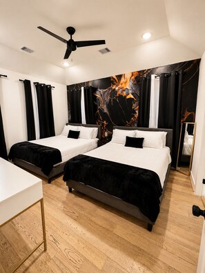 Habitació d'hotel amb dos llits, un ventilador de sostre, un mural abstracte gran i un terra de fusta.