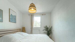 A bedroom with a bed, a hanging light fixture, a window with curtains, and a plant. - Duplex apartment with AC - 5 guests (Bias)