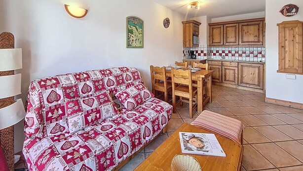 Ein gemütlicher Wohnbereich mit einer Couch und einem Esstisch, eine Küche mit Holzschränken und einer gefliesten Spritzschutzwand.