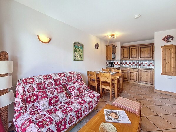 Ein gemütlicher Wohnbereich mit einer Couch und einem Esstisch, eine Küche mit Holzschränken und einer gefliesten Spritzschutzwand.