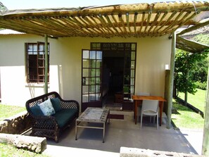 Uma área de estar coberta ao ar livre, com um sofá, mesa e cadeiras.