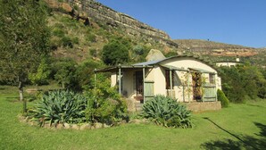 A small, single-story house with a curved roof, surrounded by a well-maintained lawn and various plants. - Mafube Mountain Retreat (Fouriesburg)
