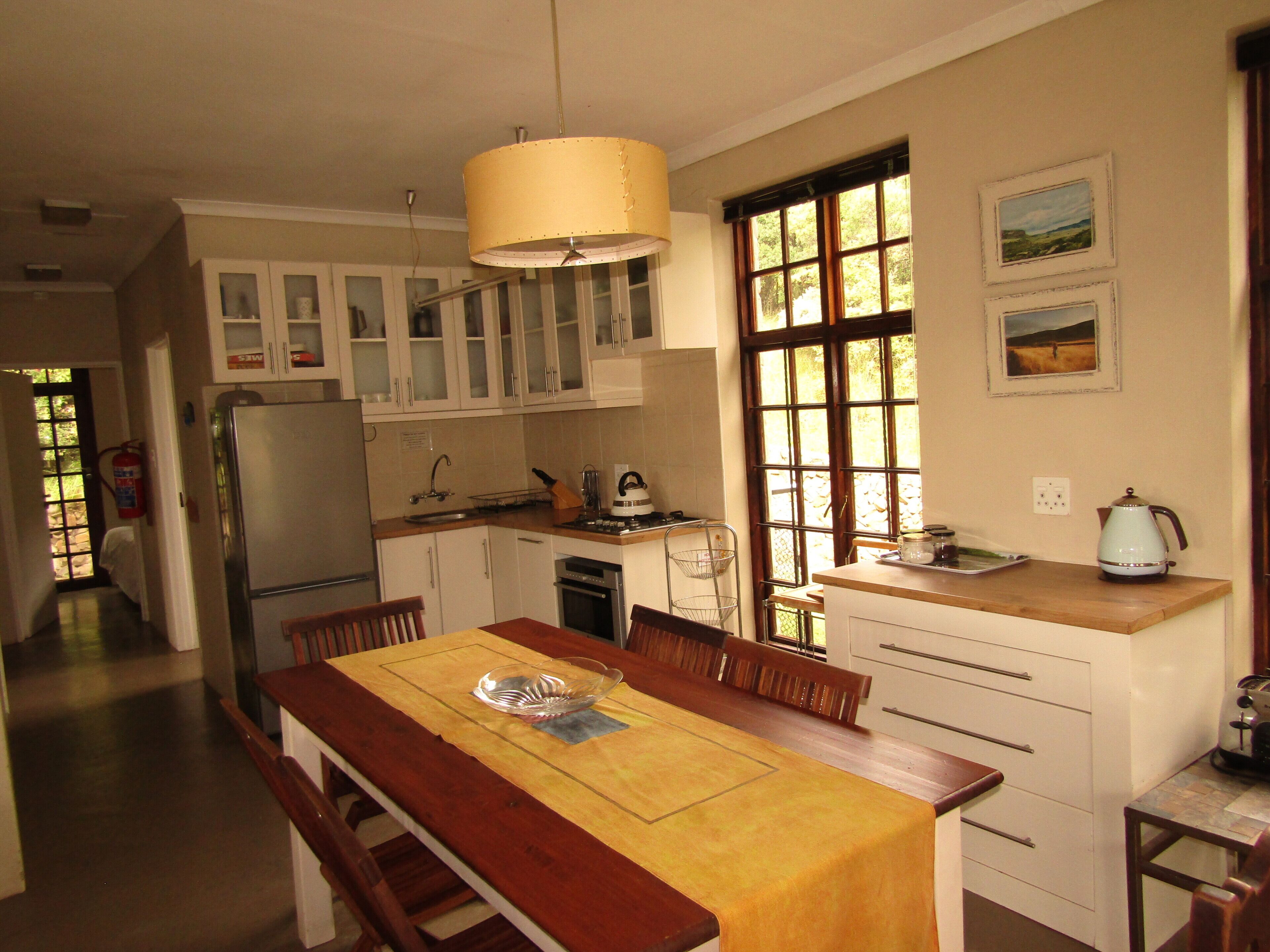 A kitchen with a dining table, cabinets, a refrigerator, and a window with artwork.