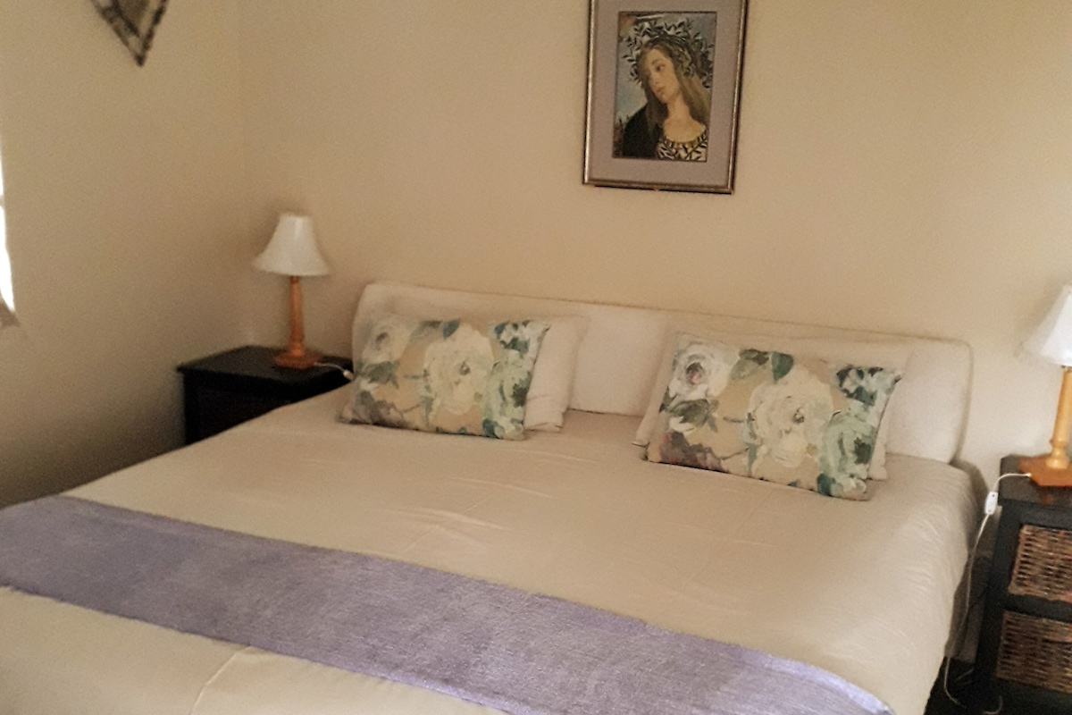 Quarto com cama, duas mesas de cabeceira, abajur, decoração em formato de coração e quadro na parede.