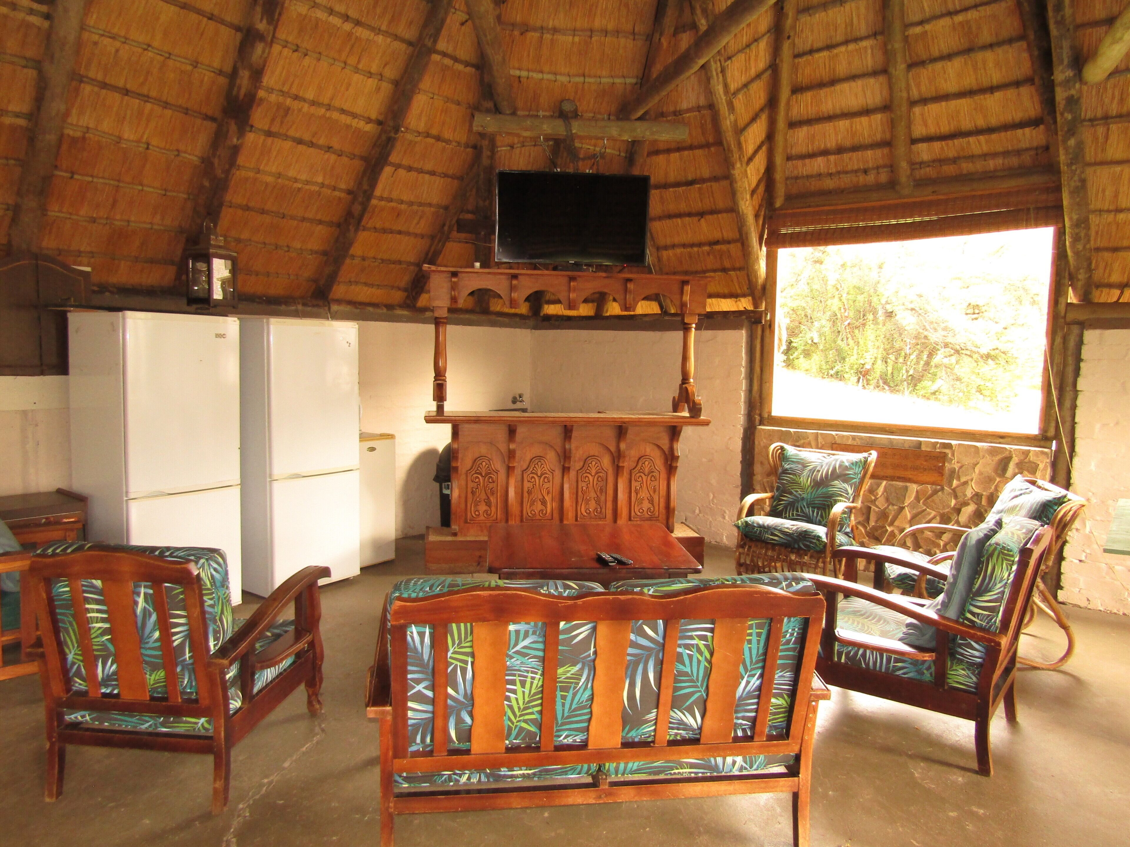 A room with a thatched roof, wooden furniture, a television, and a view of the outdoors.