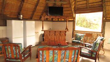 A room with a thatched roof, wooden furniture, a television, and a view of the outdoors.