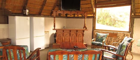 Una habitación con techo de paja, muebles de madera, televisor y vistas al exterior.