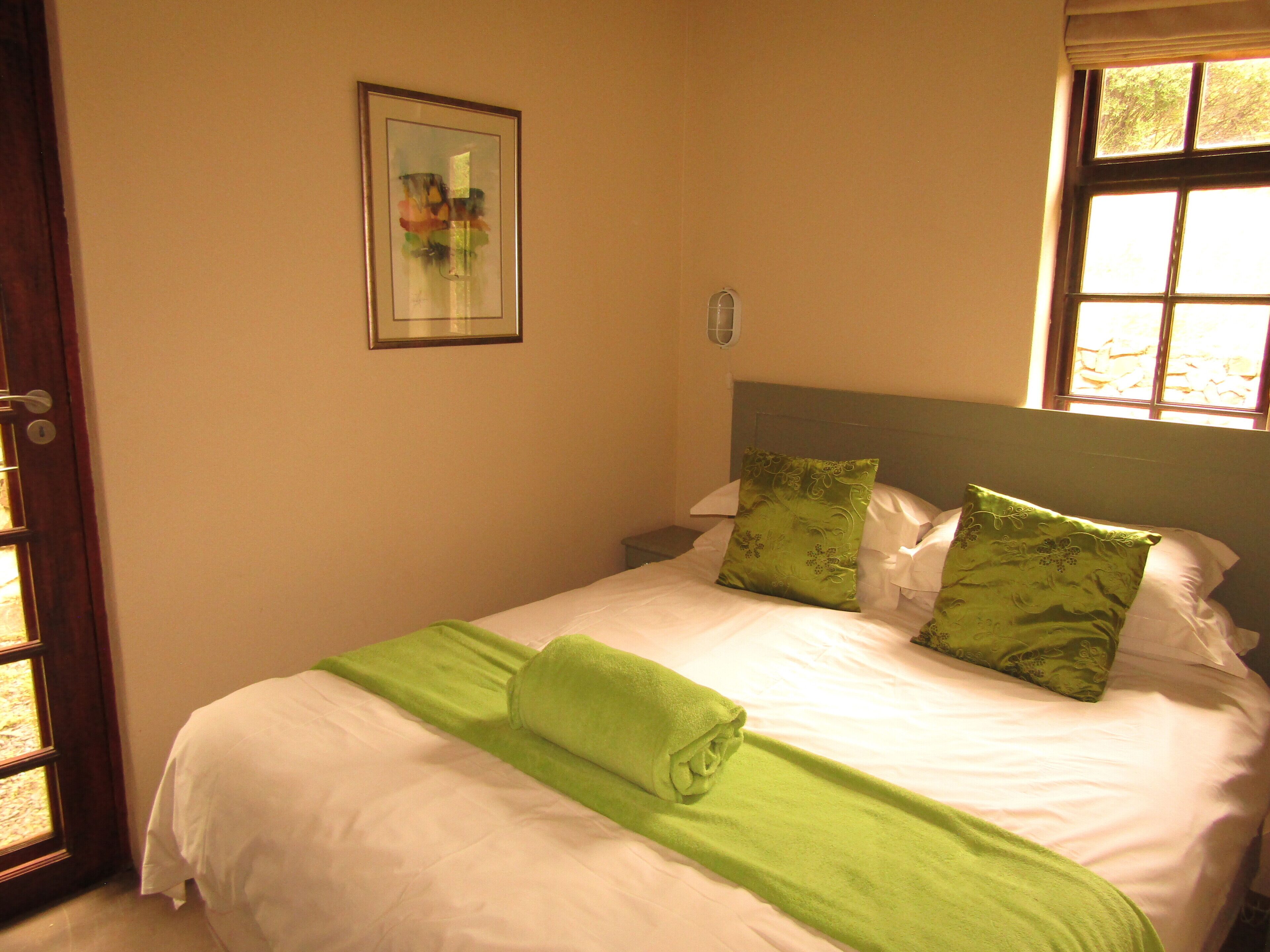 Una cama bien tendida con sábanas blancas y almohadas verdes, una toalla verde y un cuadro en la pared.