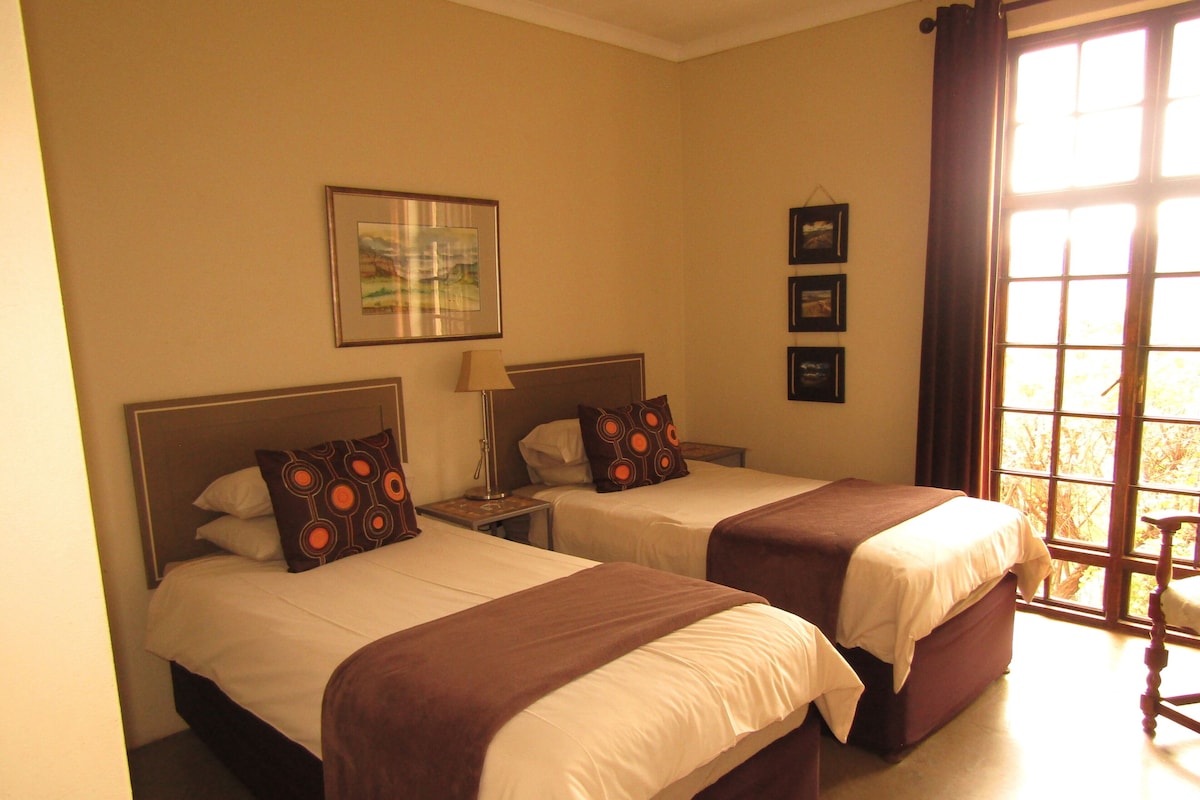 Quarto de hotel com duas camas, janela com cortinas e um quadro na parede.