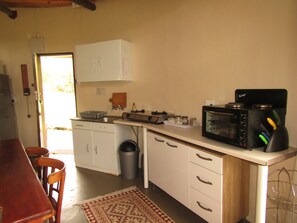 A compact kitchen with white cabinets, a microwave, a stove, and a trash can. - Mafube Mountain Retreat (Fouriesburg)