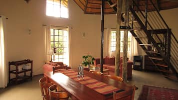 Een ruime eetruimte met een houten tafel en stoelen, een trap en grote ramen die voor natuurlijk licht zorgen.