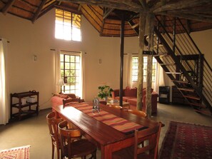 A spacious dining area with a wooden table and chairs, a staircase, and large windows allowing natural light.