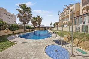 A swimming pool with a tiled deck, surrounded by palm trees and a fence, with buildings in the background. - Apartamento 'Con Terraza' con Piscina Compartida, Wi-Fi y Aire Acondicionado (Tarifa)