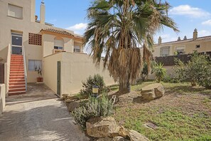 A residential area with a palm tree, a stone wall, and a building with a tiled roof. - Apartamento 'Con Terraza' con Piscina Compartida, Wi-Fi y Aire Acondicionado (Tarifa)