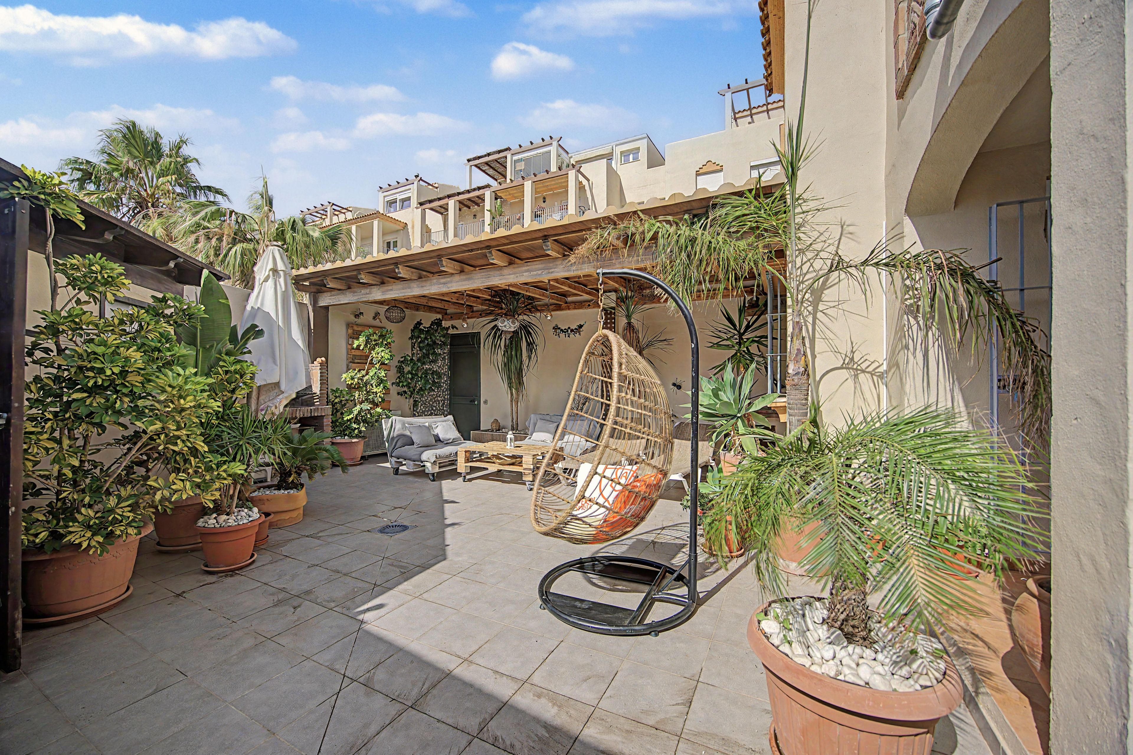 Ein Patio im Freien mit einer Hängematte, Blumentöpfen und einer Couch.