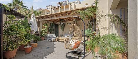 An outdoor patio area with a hanging chair, potted plants, and a sofa.