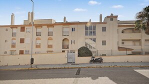 Un edificio de varios pisos con fachada plana, entrada protegida por una reja y una motocicleta estacionada.