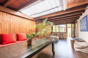 Une pièce aux murs en bois, avec un banc, des coussins rouges, une plante en pot et une table entourée de chaises.
