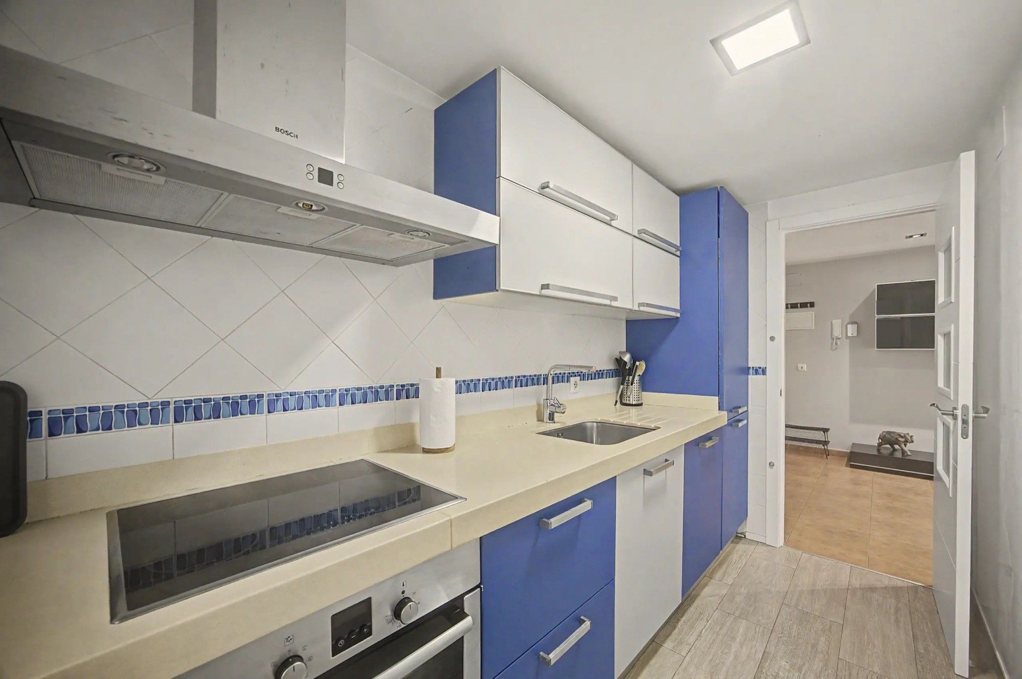A modern kitchen with white cabinets, a blue backsplash, and a stainless steel sink.