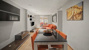 Una sala moderna con comedor, televisor de pantalla plana en la pared y un cuadro.