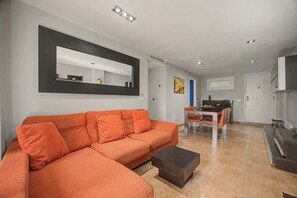 A modern living room with a sectional sofa, a dining area with a table and chairs, and a kitchen in the background. - Apartamento 'Con Terraza' con Piscina Compartida, Wi-Fi y Aire Acondicionado (Tarifa)