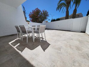 Eine Terrasse im Freien mit Tisch und Stühlen, einer weißen Wand und einer Palme.