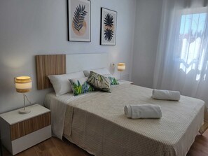 Ein ordentlich eingerichtetes Schlafzimmer mit einem Bett, zwei Nachttischlampen, einem Nachttisch und zwei an der Wand befestigten Kunstwerken.