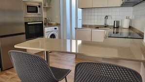 Ett modernt kök med inbyggd ugn, mikrovågsugn och tvättmaskin, en stor köksö med diskho och två stolar.