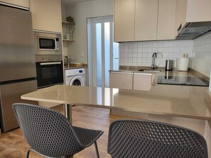 Eine moderne Küche mit Einbauofen, Mikrowelle und Waschmaschine, eine große Kücheninsel mit Spüle und zwei Stühlen.