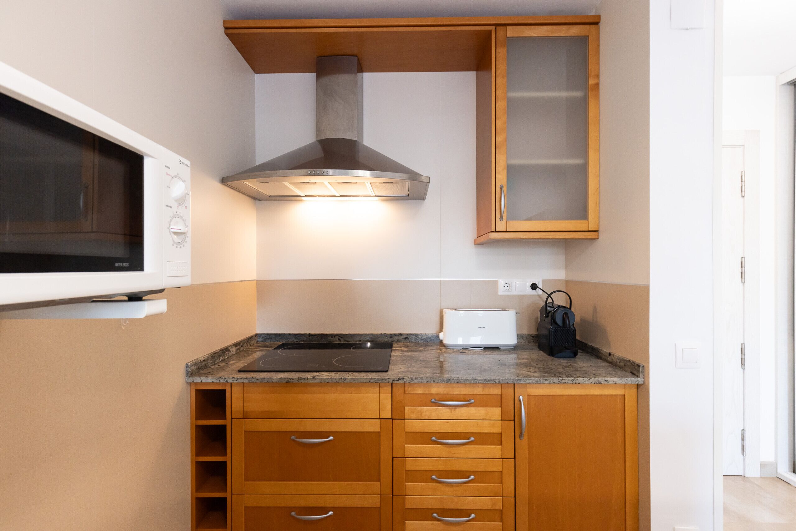 A compact kitchen with a microwave, toaster, and a range hood.