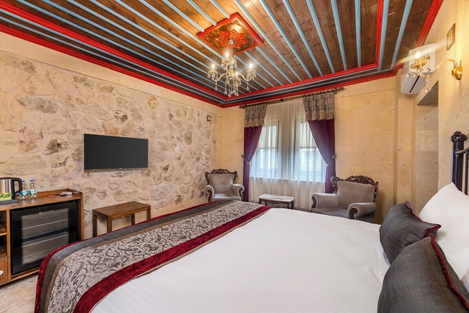 Un dormitorio con una cama grande, dos sillones, una mesita, un televisor y una pared de piedra.
