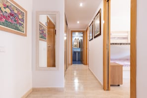 Un pasillo con una puerta de madera, un espejo, una cama y un lavabo a lo lejos.