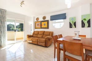 Een woonkamer met een bank, een eettafel, stoelen, kunstwerken aan de muren en uitzicht door een schuifdeur.