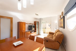 Una sala de estar con sofá, mesa de comedor y zona de cocina con armarios y televisor.