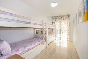 Een slaapkamer met stapelbed, raam, deur en een muur met ingekaderde foto's.