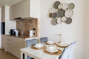Een moderne keuken met een marmeren aanrecht, een eethoek met een witte tafel gedekt voor vier personen, en een decoratieve wandcompositie.