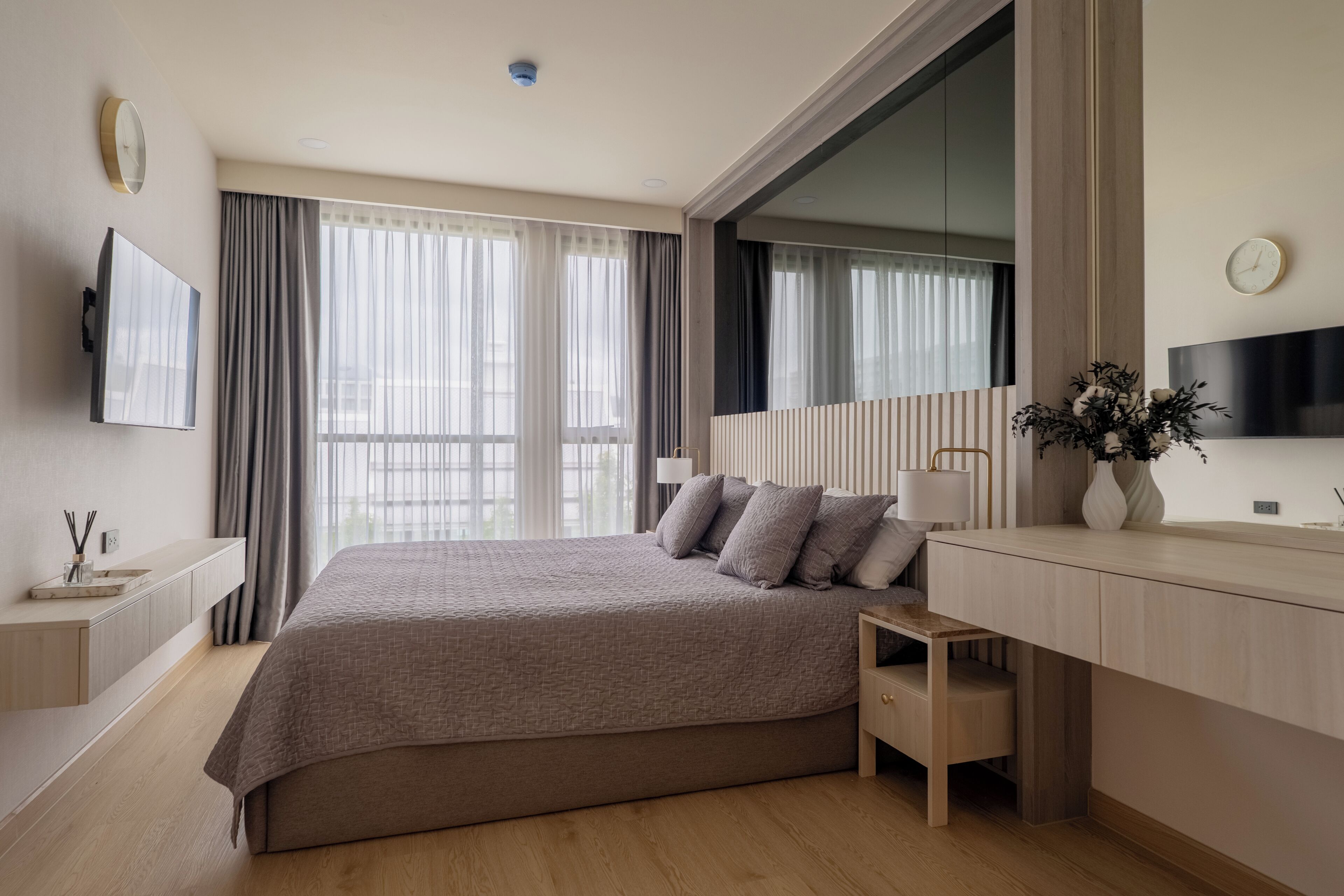 A modern hotel room with a large bed, a TV, a desk, and a window with curtains.