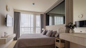 A modern hotel room with a large bed, a TV, a desk, and a window with curtains. - 1-Bedroom Ozone Apartment, Pool, Gym & Beach Shuttle (Thalang)