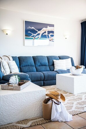 Ein Wohnzimmer mit einem blauen Sofa, einem weißen Couchtisch und einem Gemälde an der Wand.