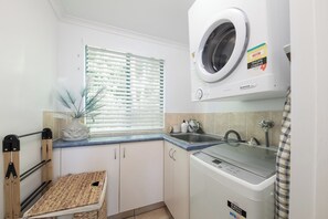 A compact laundry room with a washing machine, a dryer, and a drying rack. - Sea Crest (Airlie Beach)