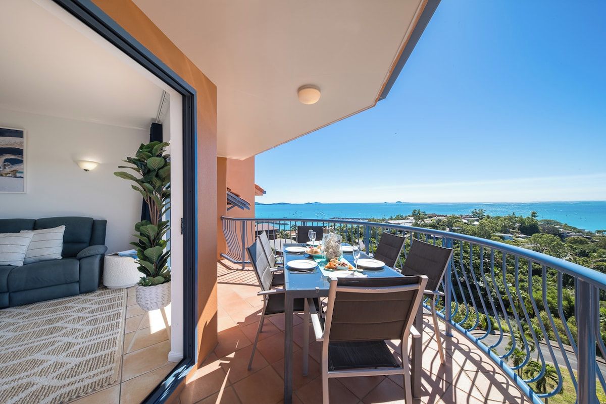 Ein Balkon mit Esstisch für zwei Personen, mit Blick auf eine Küstenlandschaft.